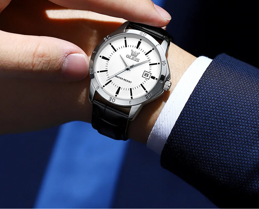 Hand wearing a black wristwatch with a white face, set against a blue background, featuring the OLEVS brand.