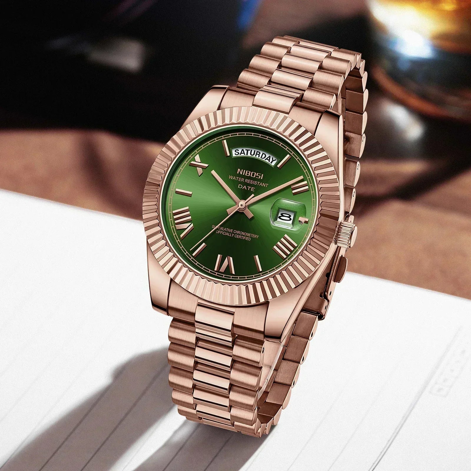 Rose gold watch with green dial on a white surface