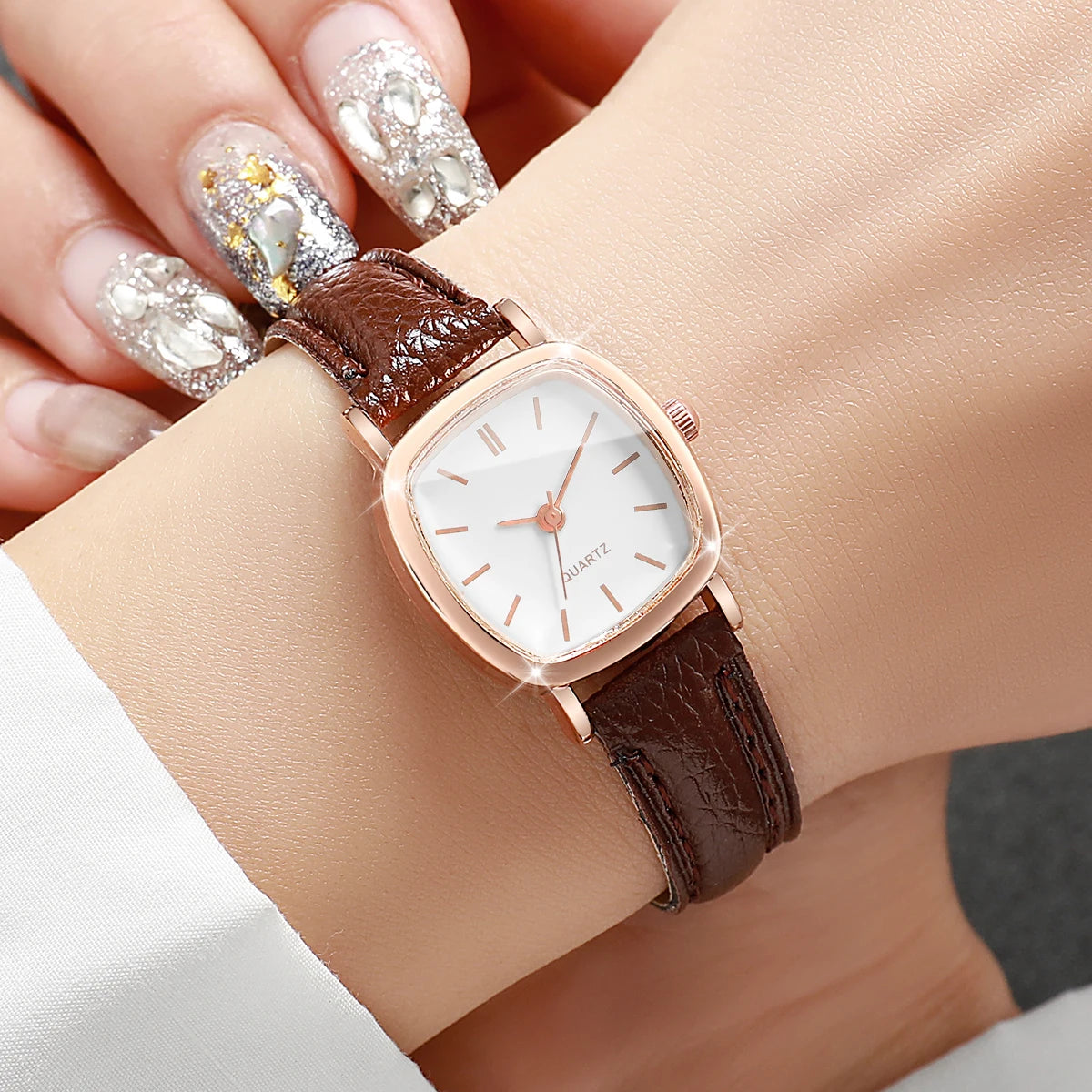 Wristwatch with brown leather strap and rose gold case on a wrist with decorative nails.