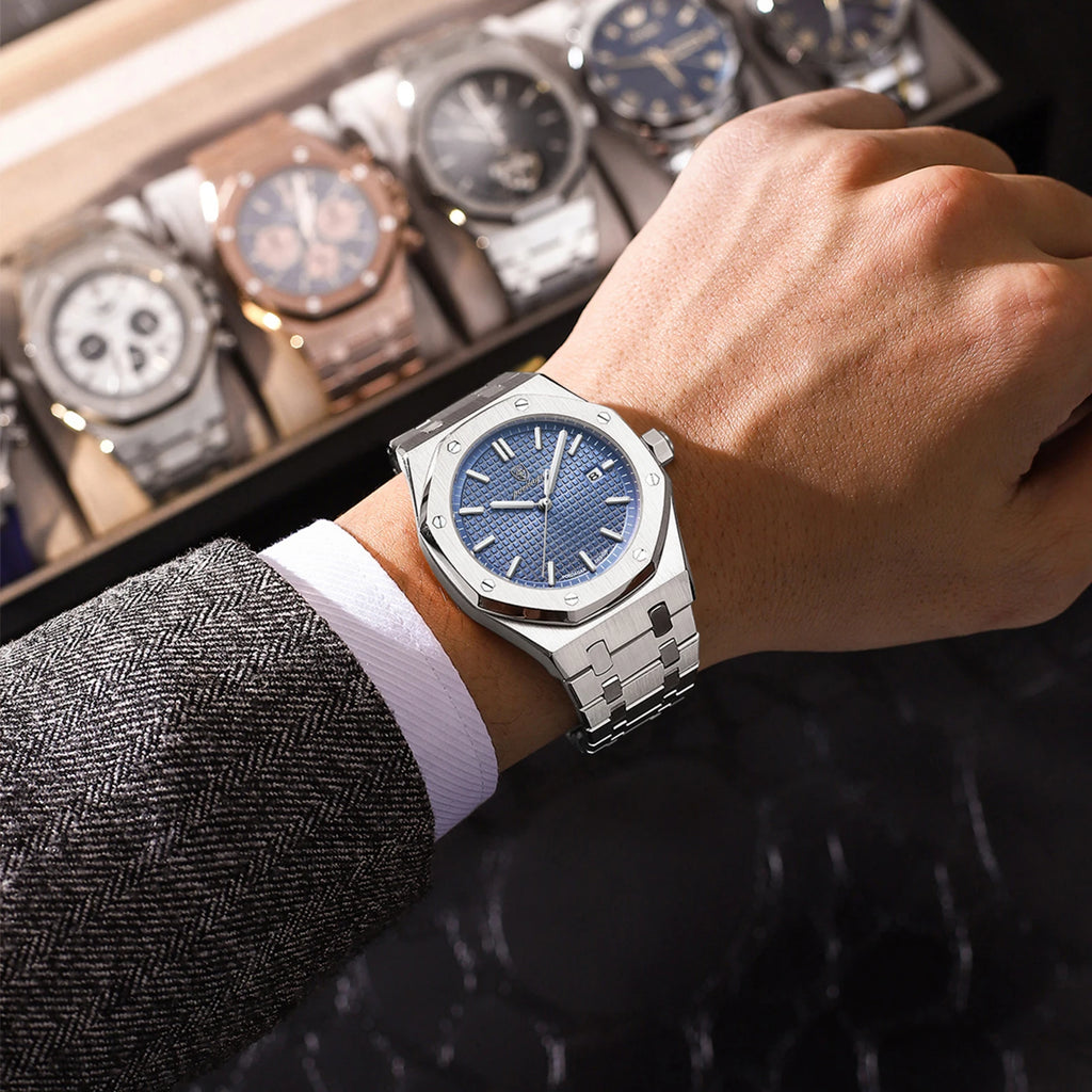 Hand wearing a silver watch with a blue face, with a display of other watches in the background.