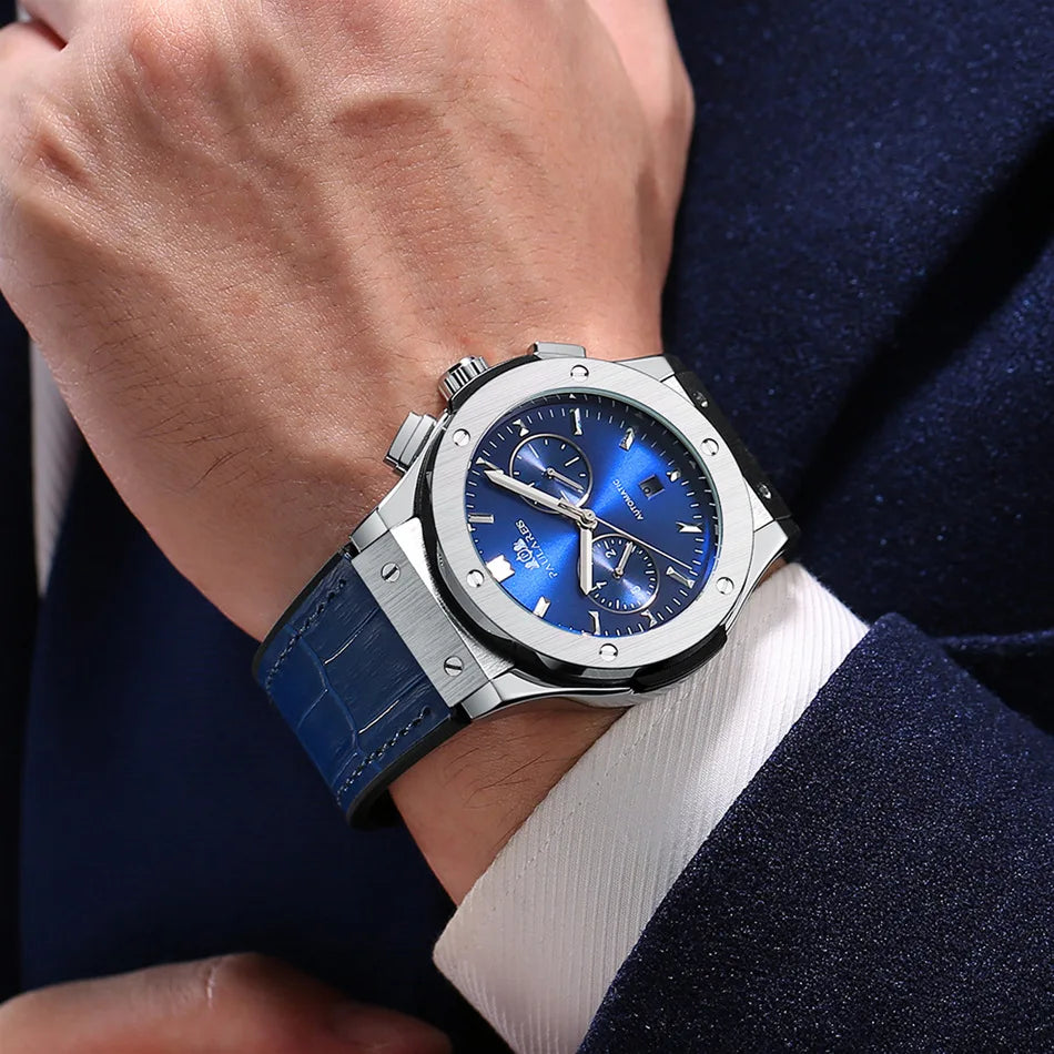 Blue watch with silver case on a person's wrist wearing a dark suit and white shirt.