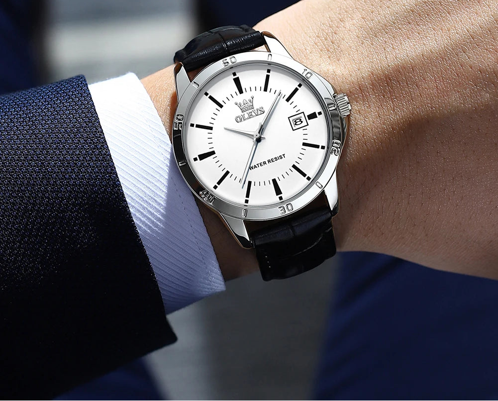 Wristwatch with black strap and white dial on a person's wrist, brand 'OLEVS' visible.