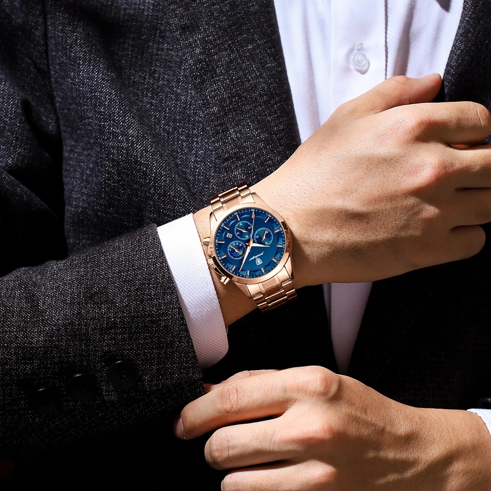 Person wearing a rose gold watch with a blue face on a dark suit background
